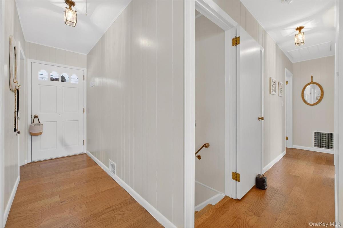 Hall featuring light wood-type flooring, an upstairs landing, and wood walls