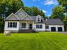 Stunning front exterior showcasing timeless architectural details, covered front porch, oversized two-car garage, mature trees, and expansive lawn.