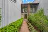 Brick pathway entry framed by manicured hedges and established shrubs, leading to a recessed entryway with a full-light door