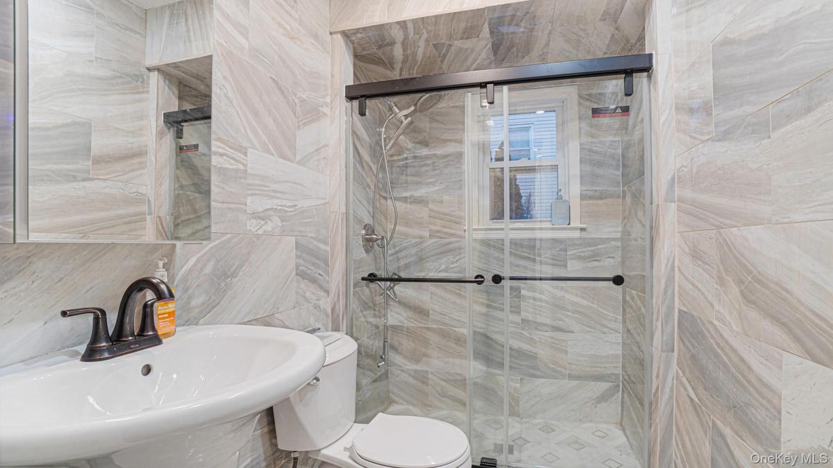 Bathroom with a shower stall, toilet, a sink, and tile walls