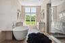 Primary bathroom with twin vanities, soaking tub, large glass shower with dual rain shower heads, separate lavatory and radiant heated bluestone floor