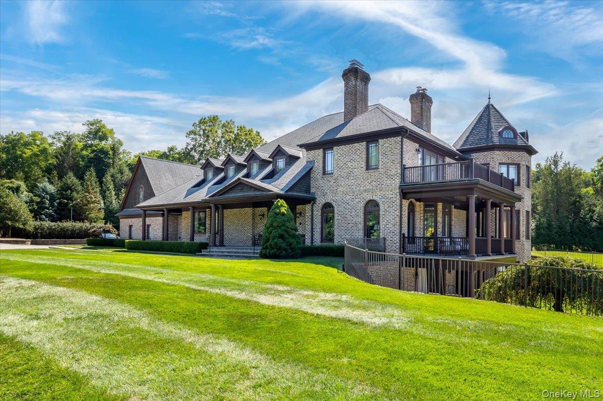 View of front of property with brick siding, a front yard, a chimney, and a balcony