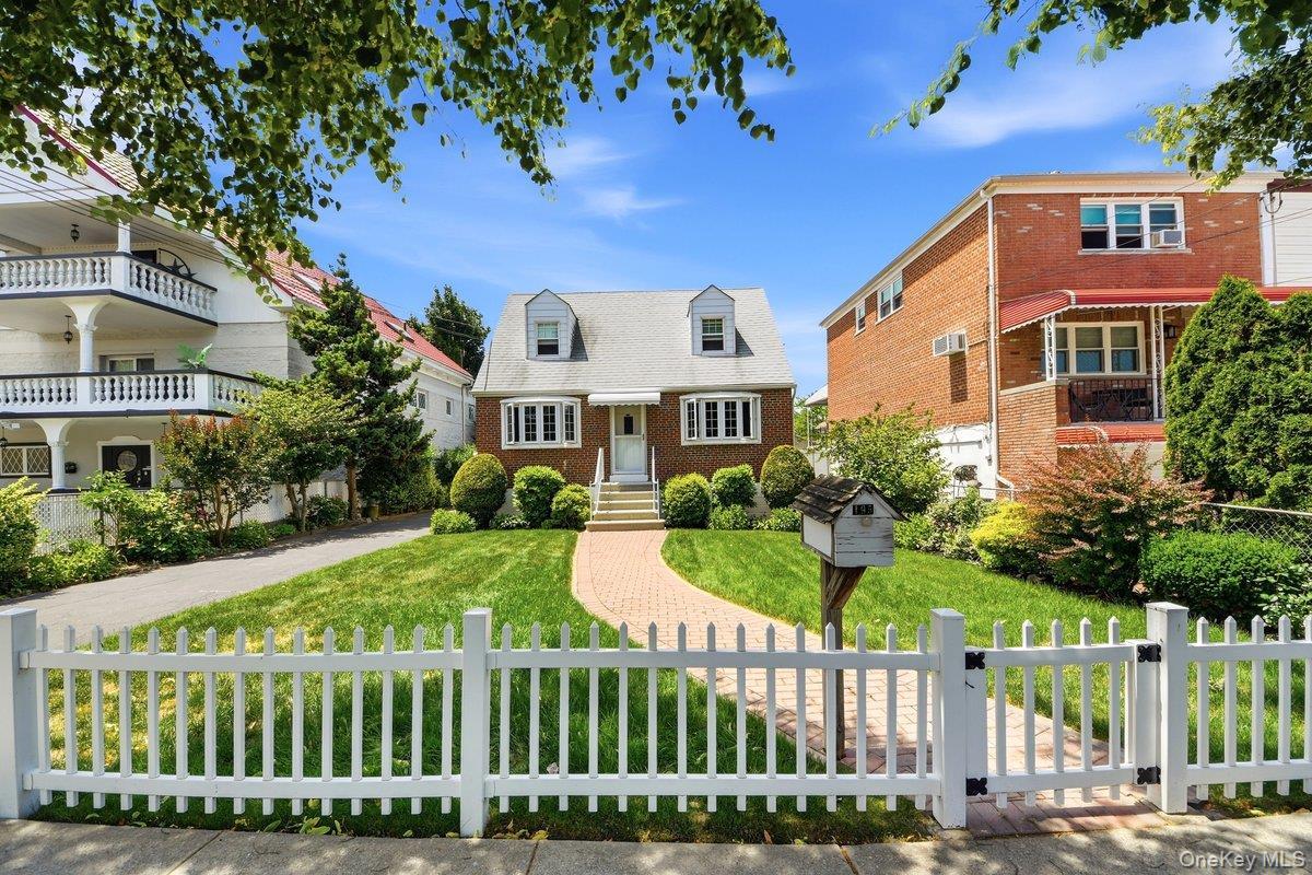 Brick exterior home featuring a gabled roof, white picket fence, and a curved brick pathway