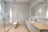 En-suite bath with full-height white marble tile walls and floors, frameless glass walk-in shower, smart toilet, floating vanity with warm stone count