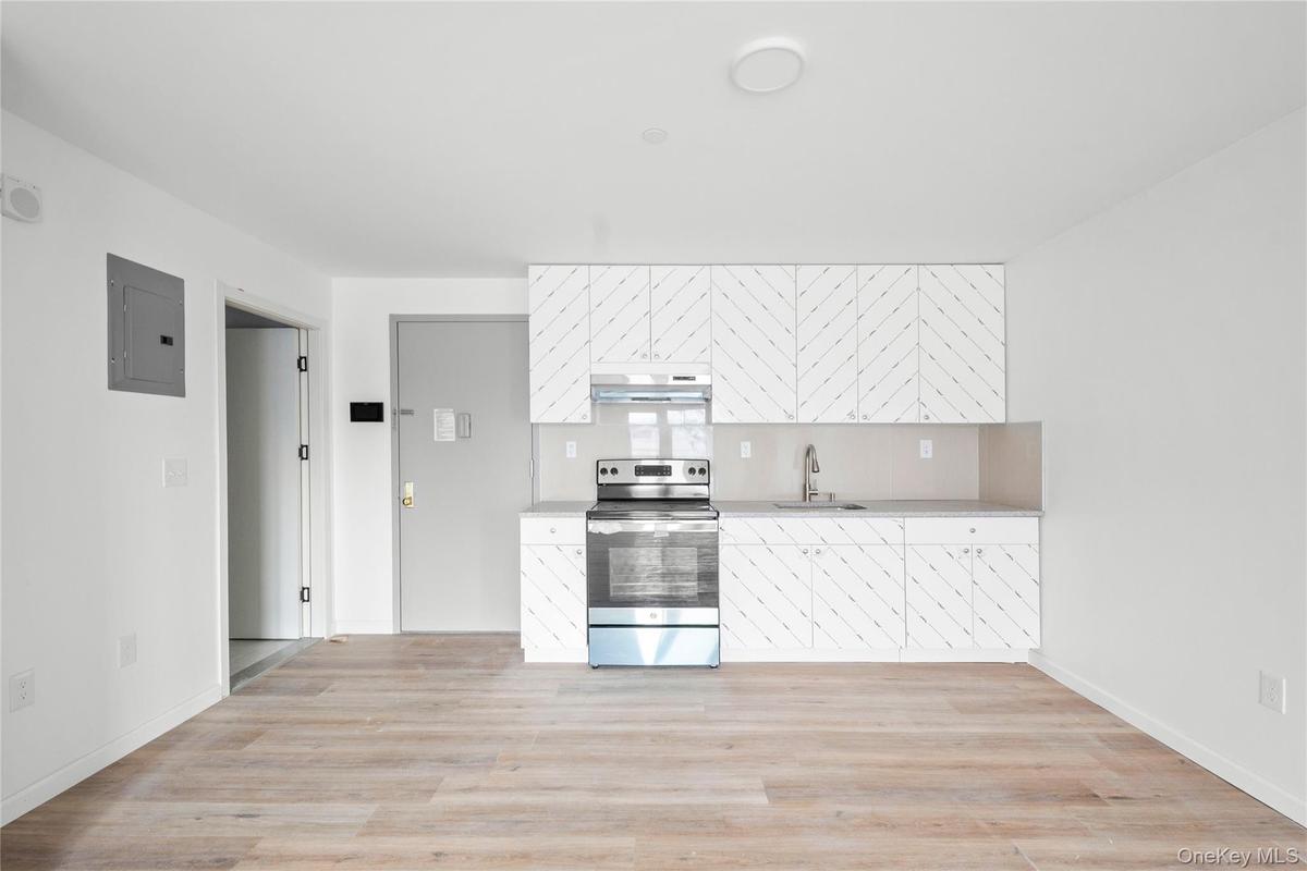 Kitchen featuring stainless steel electric range oven, electric panel, white cabinetry, light wood-type flooring, and tasteful backsplash