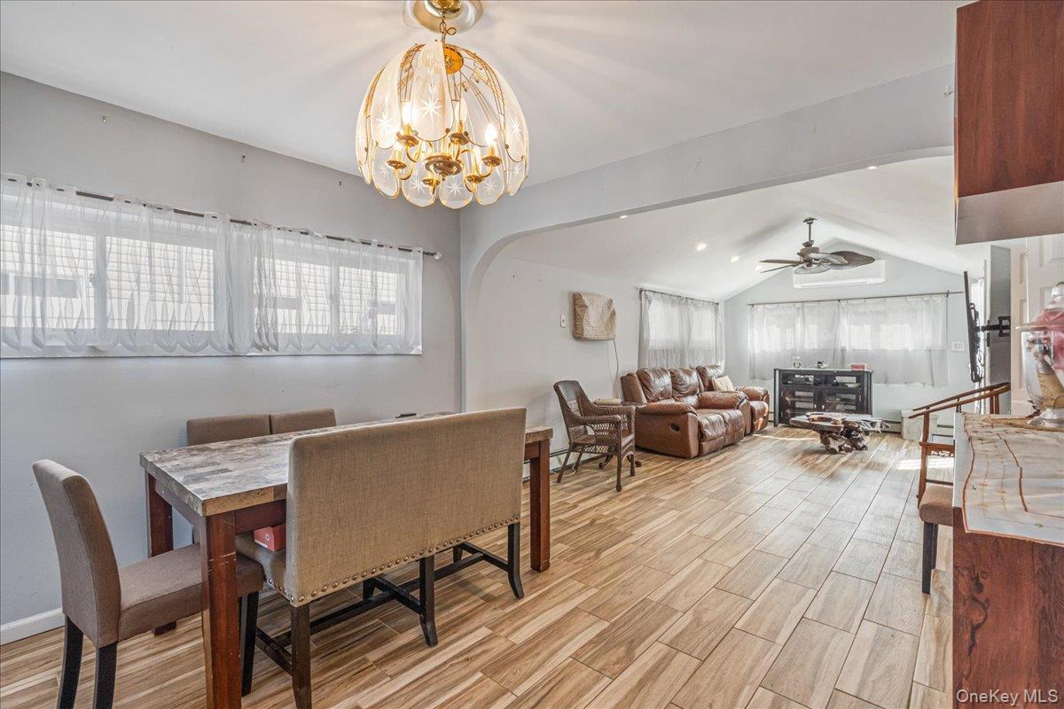 Dining space featuring wood tiled floors, vaulted ceiling, arched walkways, ceiling fan, and suspended lighting