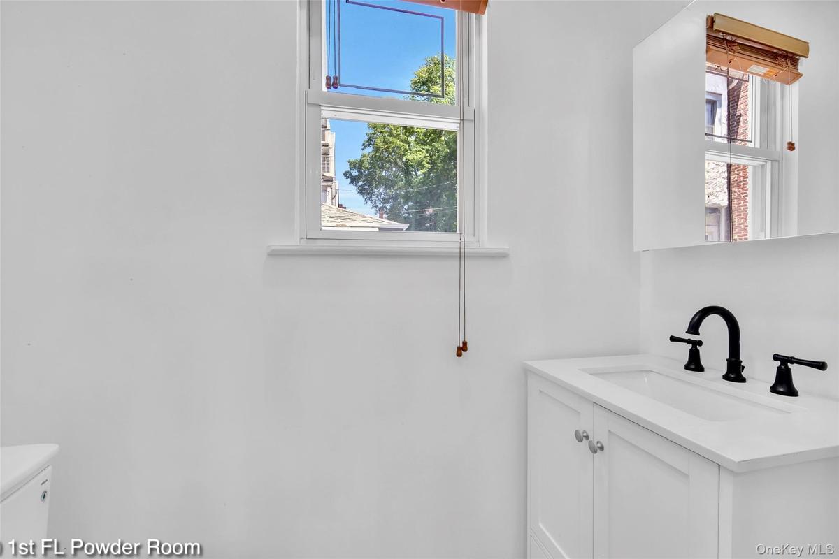Powder room featuring a white single-sink vanity with matte black faucet, white shaker-style cabinetry with silver hardware, an integrated sink, and a