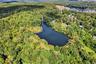 Aerial view of property and surrounding area featuring a nearby body of water and a heavily wooded area