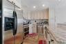 Kitchen featuring wood-finish flooring, stainless steel appliances, light-toned cabinetry with dark hardware, a stone countertop, and a tiled backspla