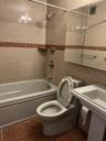 Bathroom featuring tiled shower / bath combo, toilet, and tile walls