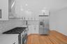 Kitchen with appliances with stainless steel finishes, white cabinetry, wall chimney range hood, light wood-style flooring, and backsplash