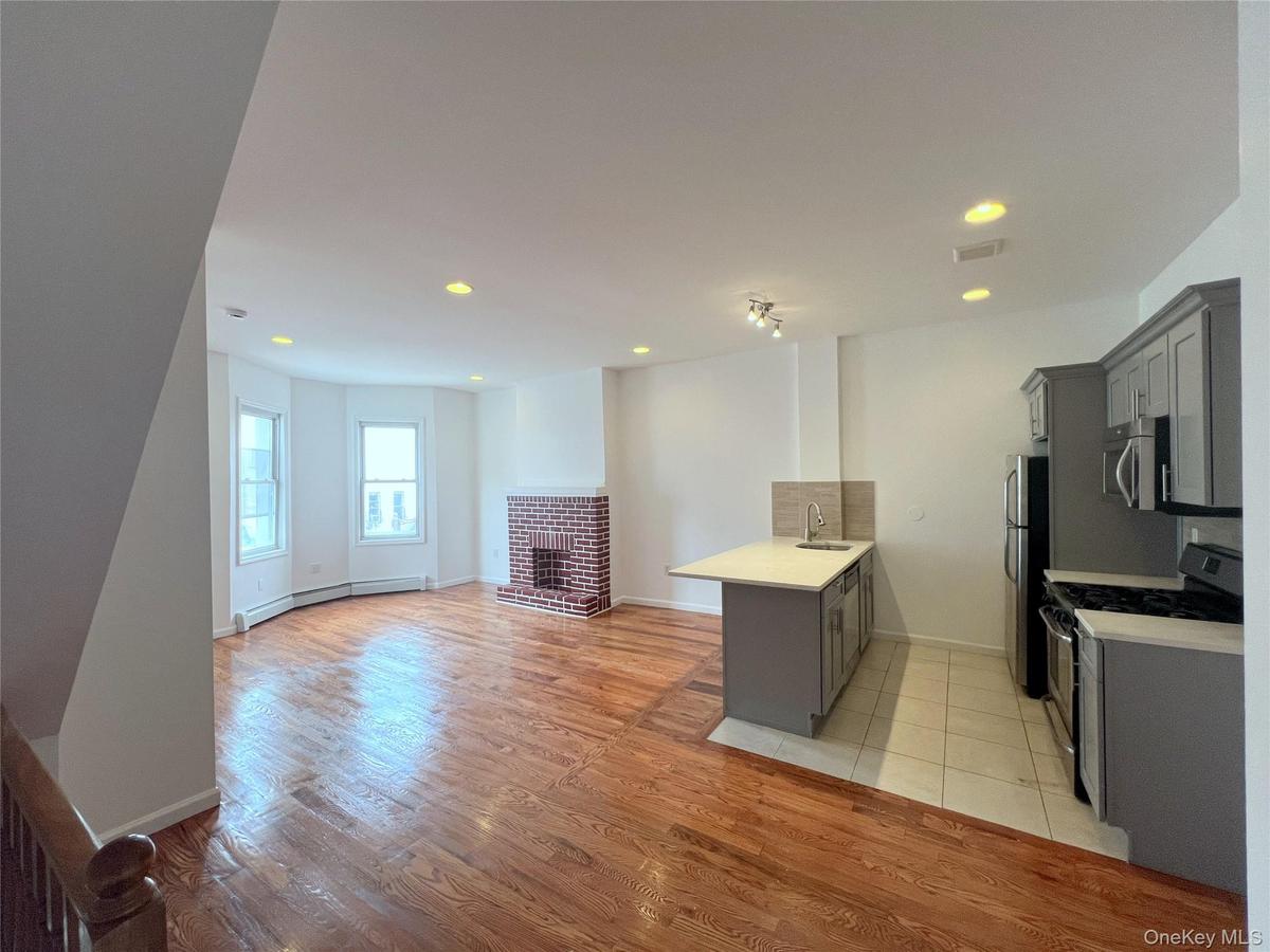 Kitchen featuring stainless steel appliances, gray cabinets, a peninsula, light countertops, and a brick fireplace