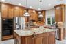 Kitchen featuring light tile patterned floors, brown cabinetry, light stone countertops, appliances with stainless steel finishes, and recessed lighti