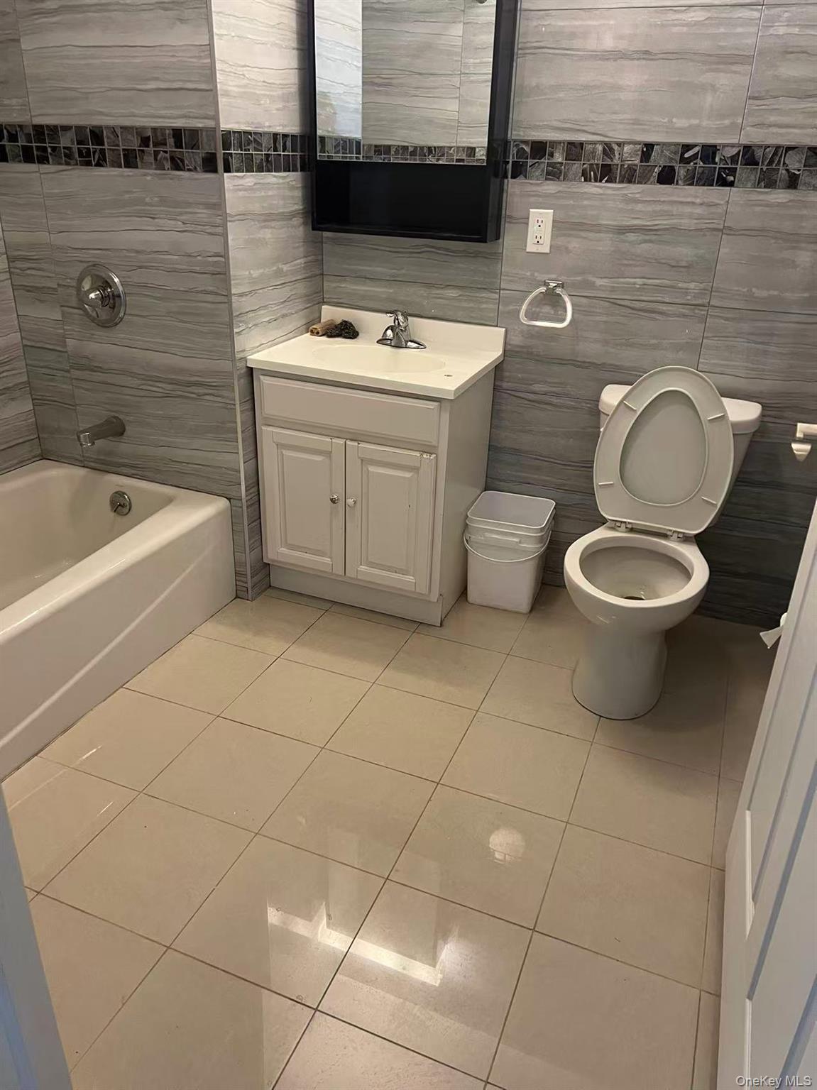 Bathroom featuring tile patterned flooring, toilet, vanity, tile walls, and washtub / shower combination