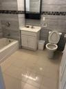Bathroom featuring tile patterned flooring, toilet, vanity, tile walls, and washtub / shower combination