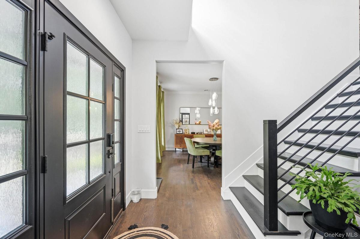 A welcoming, light-filled foyer featuring double entry doors, rich hardwood floors and a sleek modern staircase with black railings. The open sightlin