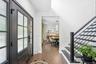 A welcoming, light-filled foyer featuring double entry doors, rich hardwood floors and a sleek modern staircase with black railings. The open sightlin