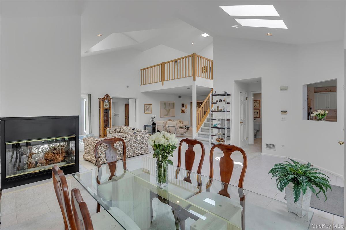 Dining area featuring a glass-top table, a black-framed fireplace, vaulted ceilings, skylights, and a partial view of a staircase with wood railing