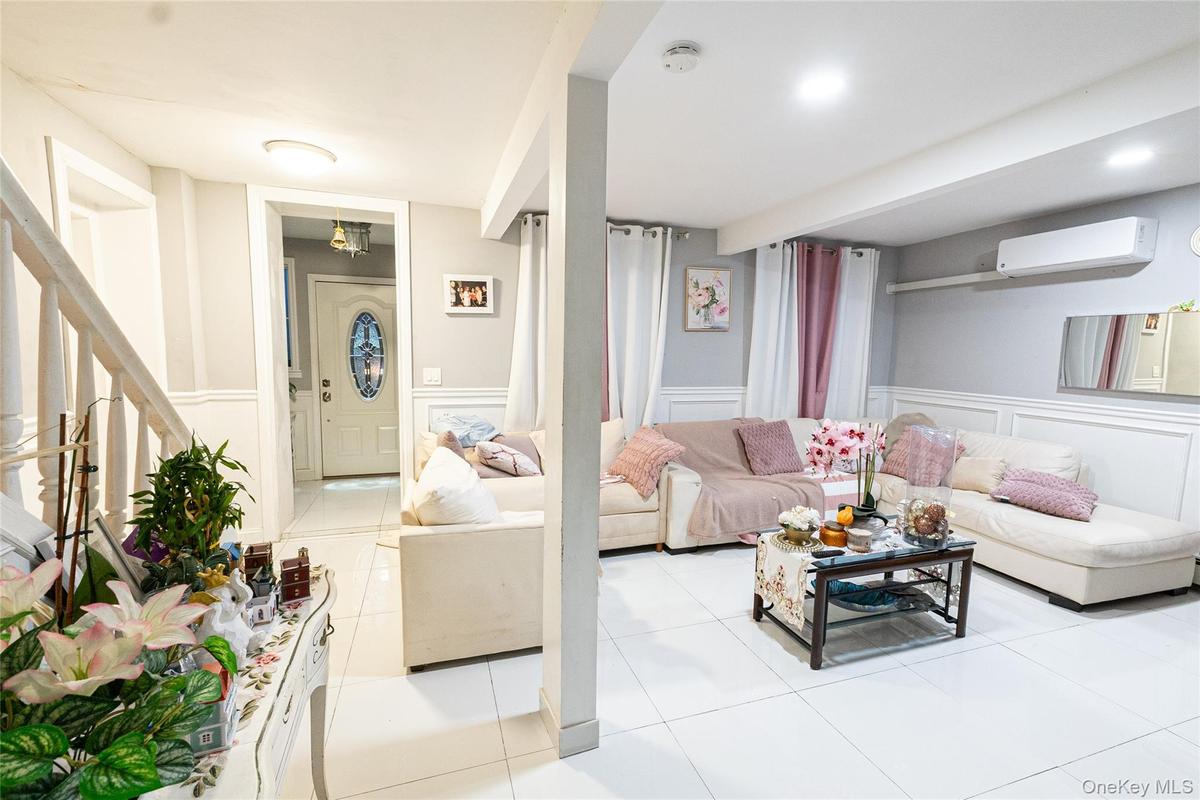 Living area with a decorative wall, a wainscoted wall, light tile patterned floors, a wall unit AC, and stairway