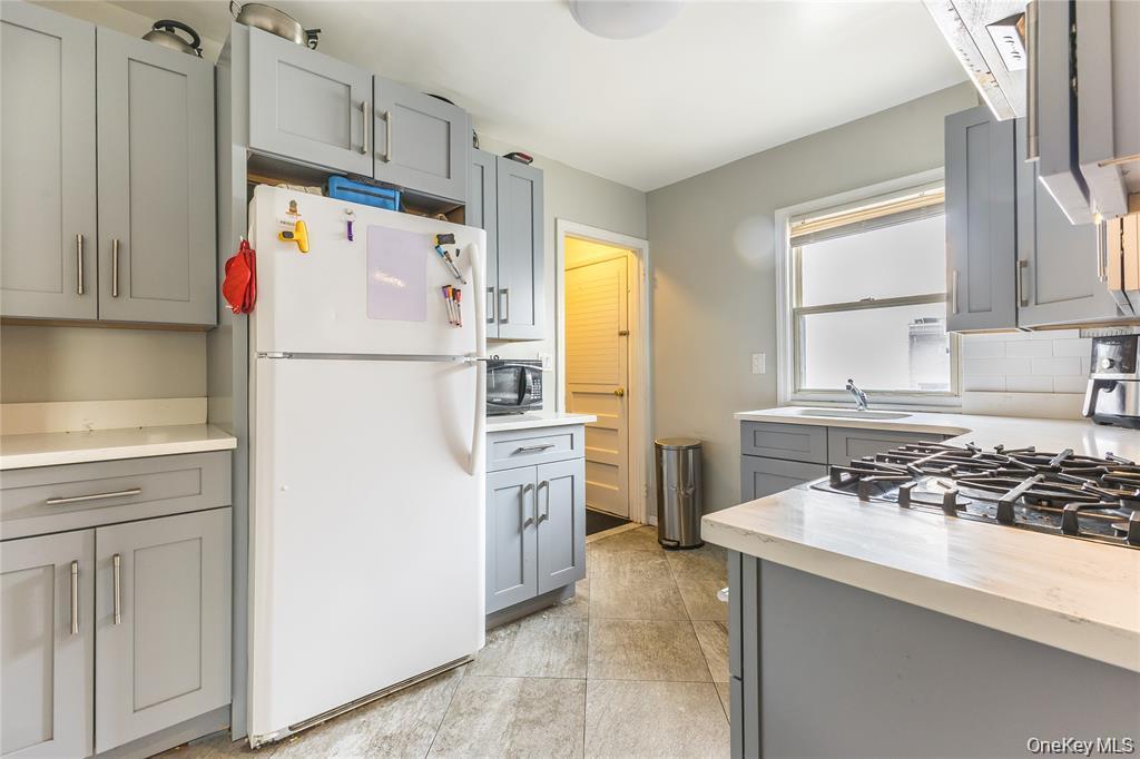 Kitchen featuring gray cabinets, freestanding refrigerator, light tile patterned floors, black microwave, and backsplash