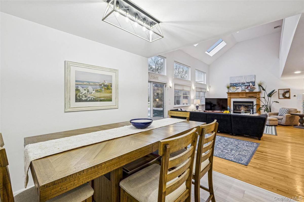 Dining space featuring a glass covered fireplace, high vaulted ceiling, light wood-style floors, and a skylight