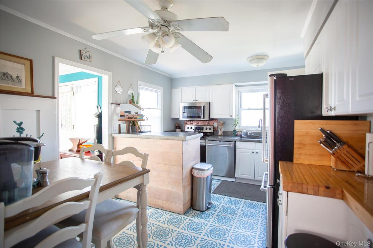 Kitchen with white cabinets, appliances with stainless steel finishes, dark countertops, ornamental molding, and ceiling fan