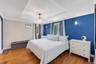 Bedroom featuring wood-finish flooring, a tray ceiling with a chandelier, crown molding, two windows with curtain rods, and two wall sconces