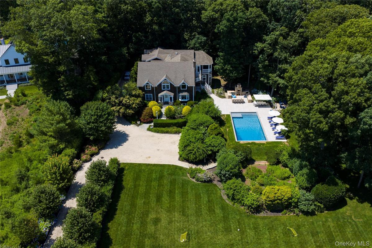 Expansive property featuring a dark-sided residence with white trim, a large in-ground swimming pool, a spacious patio area, a gravel driveway, and ex