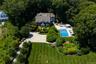 Expansive property featuring a dark-sided residence with white trim, a large in-ground swimming pool, a spacious patio area, a gravel driveway, and ex