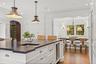 Elegant white kitchen with oversized island, pendant lighting, and hardwood floors. Opens to a bright dining nook, perfect for everyday living and ent