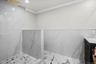 Walk-in shower with marble-style tile, frameless half wall, and rainfall showerhead for a spa-inspired experience.
