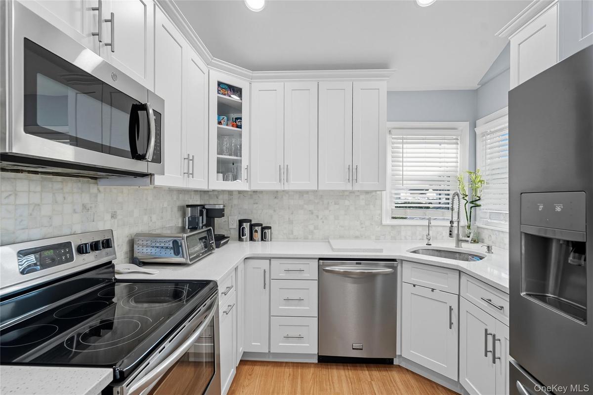 Kitchen with appliances with stainless steel finishes, white cabinetry, backsplash, glass insert cabinets, and recessed lighting