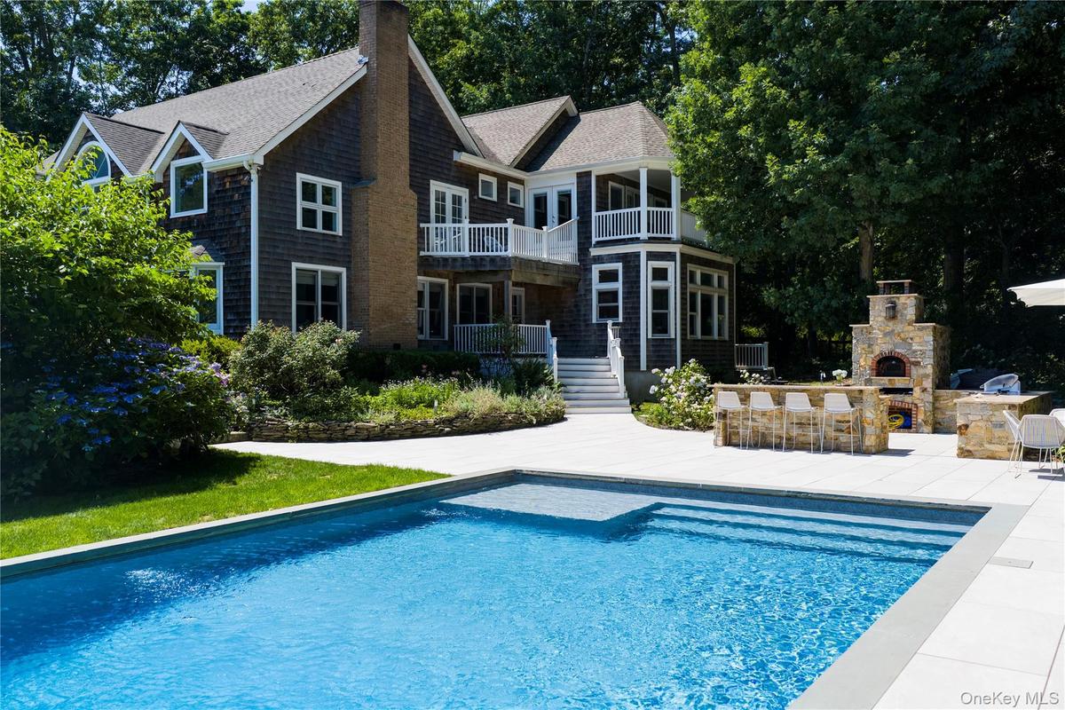 In-ground swimming pool with integrated steps and sun shelf, expansive patio, and an outdoor kitchen featuring a built-in pizza oven