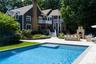 In-ground swimming pool with integrated steps and sun shelf, expansive patio, and an outdoor kitchen featuring a built-in pizza oven