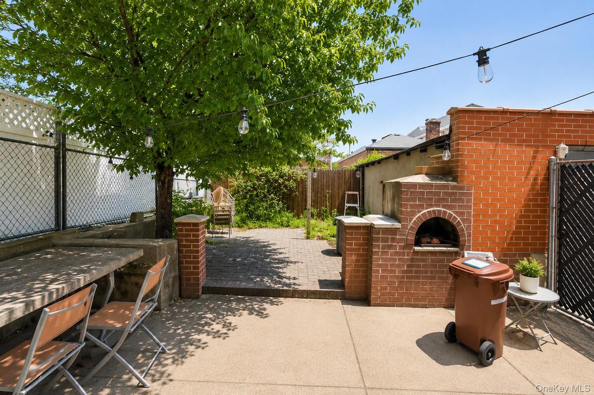 Spacious outdoor area featuring a built-in brick oven, concrete patio, and mature tree with string lighting