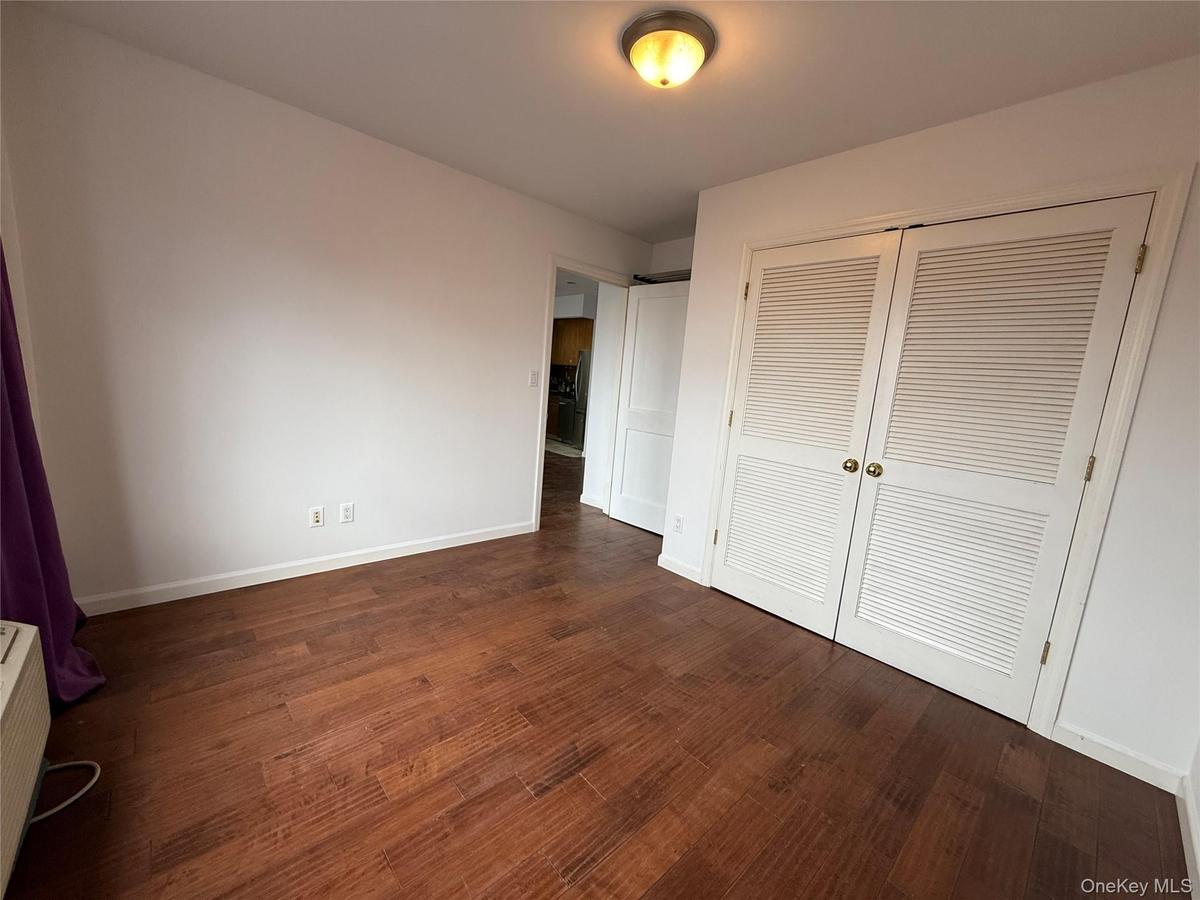 Unfurnished bedroom featuring dark wood finished floors, a closet, and a wall mounted air conditioner