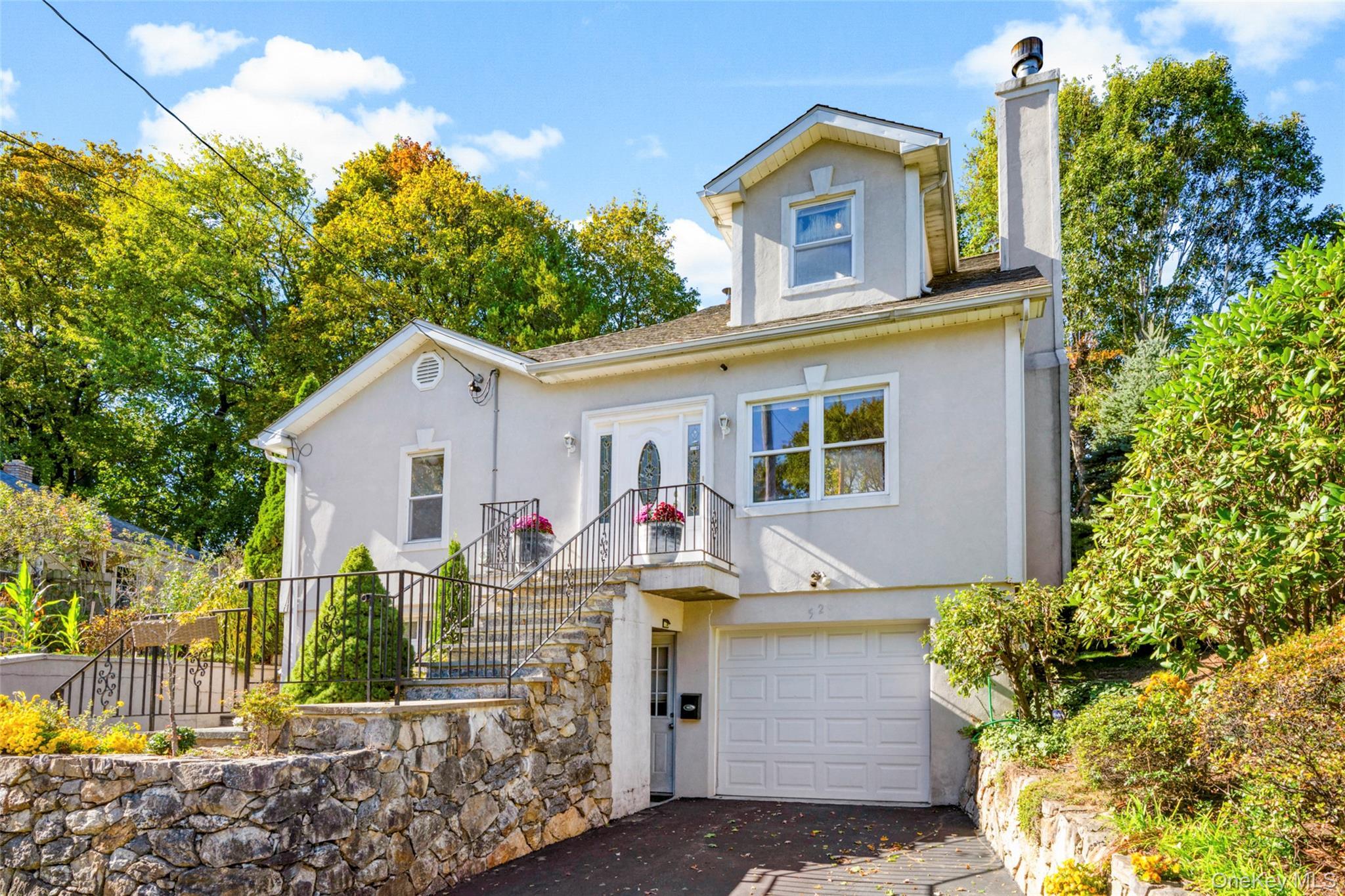 View of front facade with stucco siding, a chimney, 2 car attached garage, and driveway.