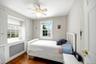 Hardwood flooring grounds this first floor bedroom, featuring two windows with white trim, a built-in radiator cover