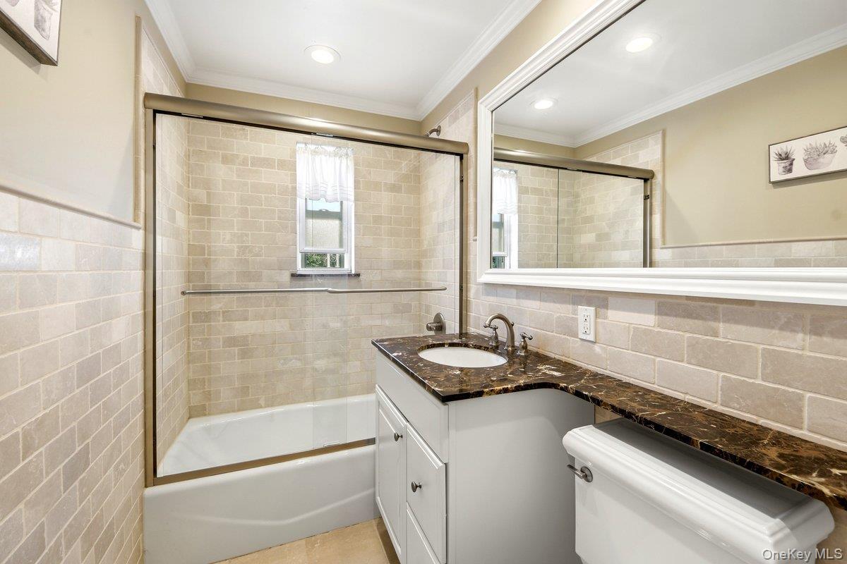 1st fl Bathroom featuring a tiled tub-shower combination with sliding glass doors, a vanity with a dark marbled countertop and an integrated sink, a l