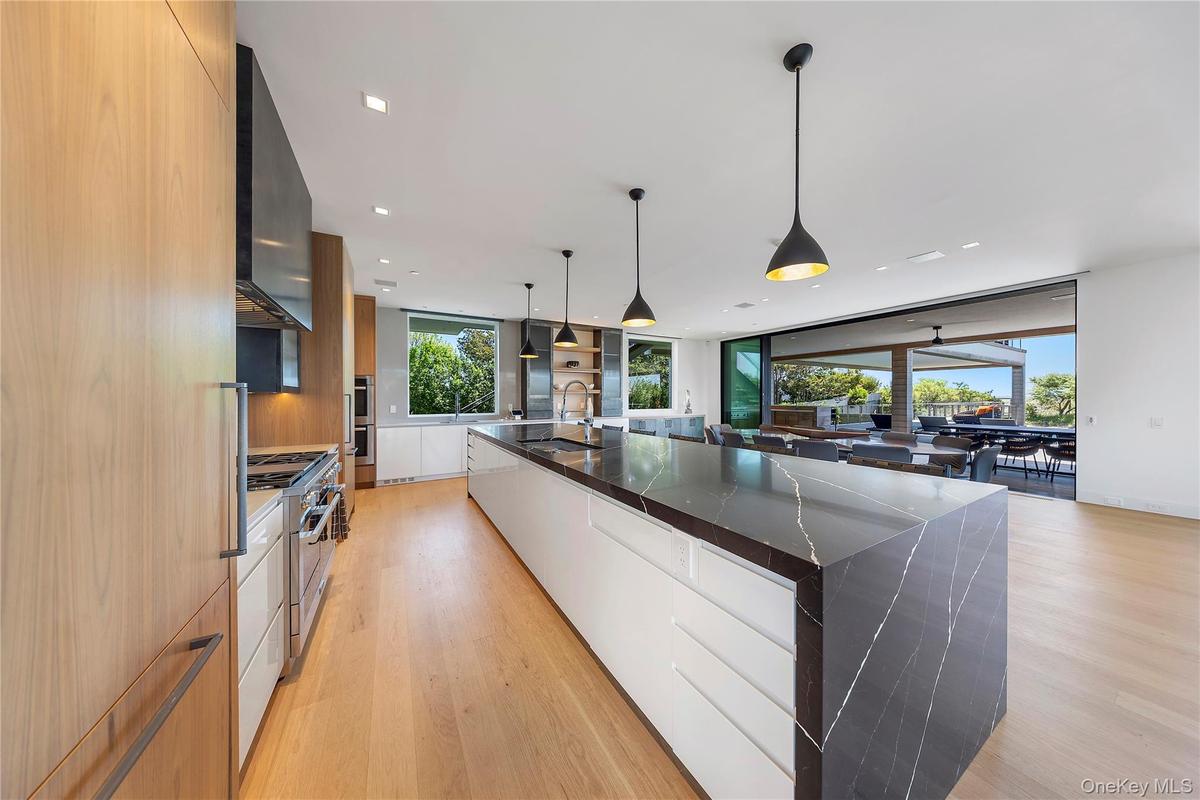 Kitchen with modern cabinets, light wood-style floors, dark stone countertops, decorative light fixtures, and floor to ceiling windows