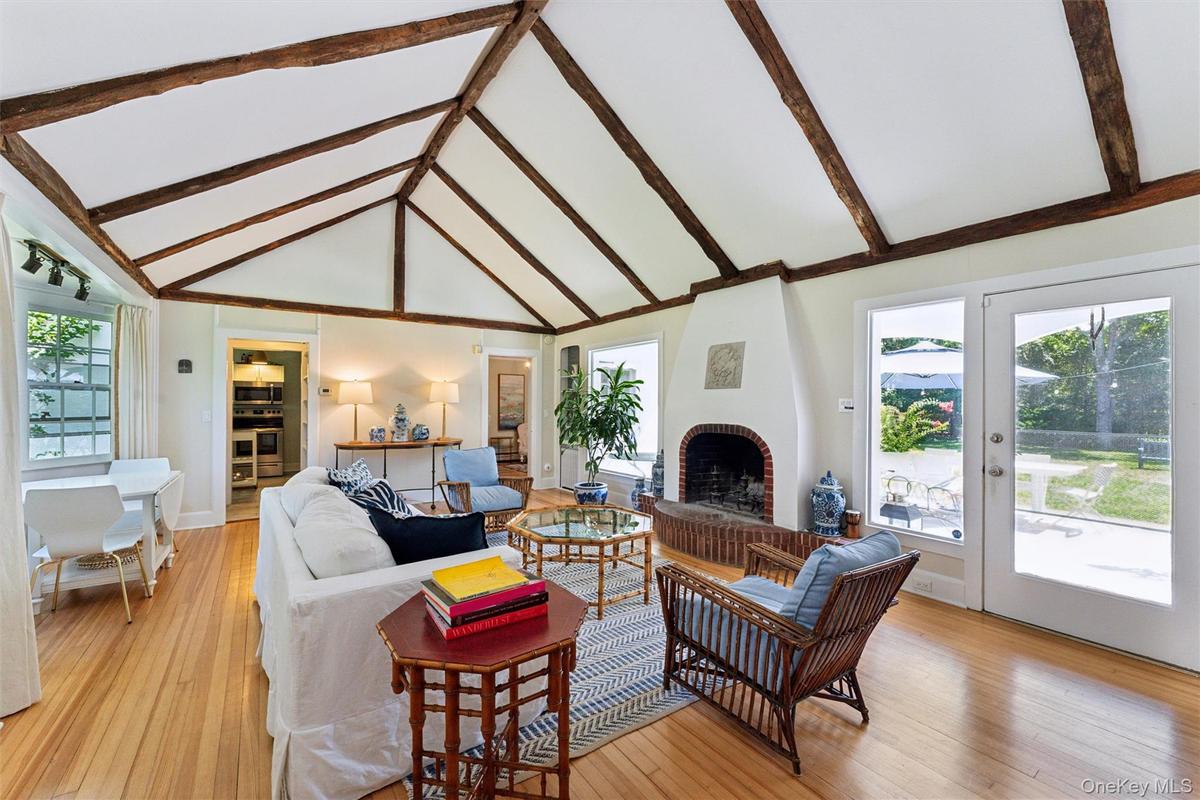 Living room with healthy amount of natural light, light wood-style floors, high vaulted ceiling, beam ceiling, and a brick fireplace