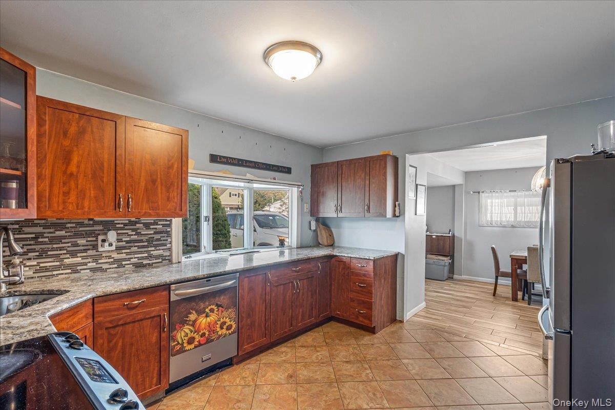 Kitchen featuring stainless steel appliances, glass fronted cabinets, light stone counters, and decorative backsplash