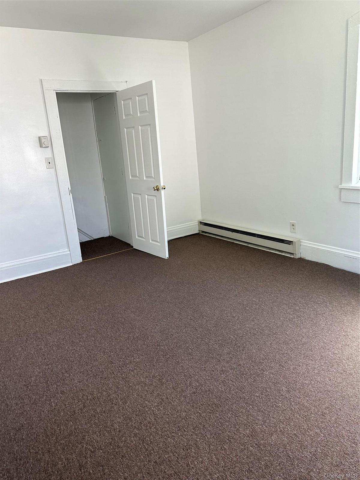 Carpeted spare room featuring a baseboard radiator