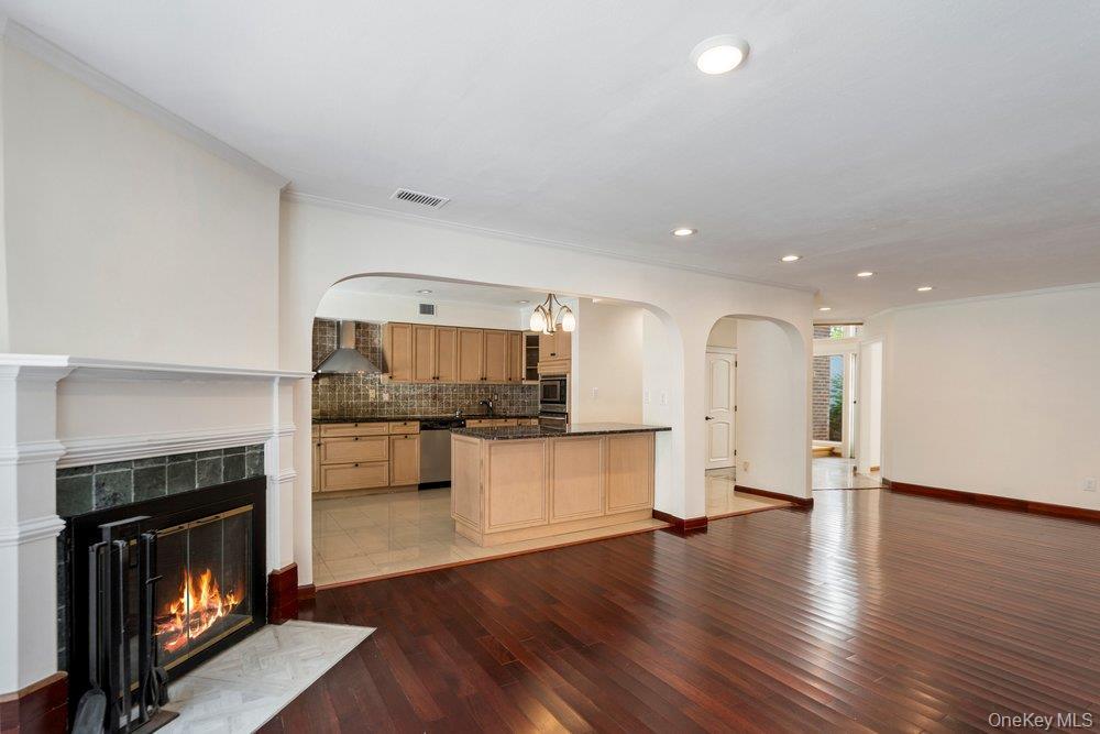 Spacious interior showcasing rich wood-finish flooring, a classic fireplace with a detailed mantel and tile surround, and recessed lighting