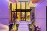 Double-height glass-and-steel entry with marble steps, stainless steel railings, spiral topiaries, and open view into grand two-story foyer interior.