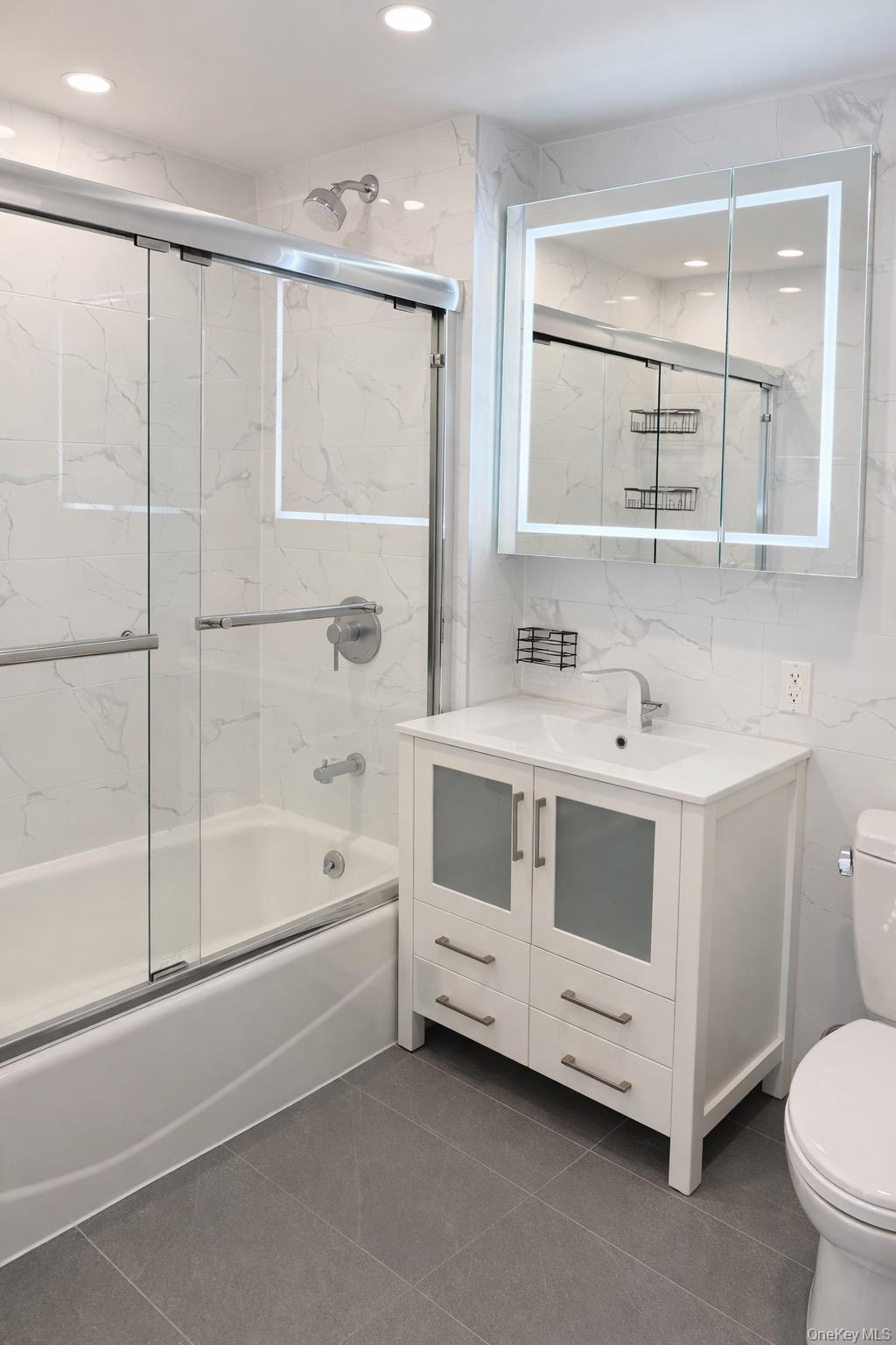 Bathroom featuring tile walls, combined bath / shower with glass door, vanity, dark tile patterned flooring, and recessed lighting