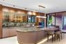 Designer kitchen with curved stone island, under-island LED lighting, fluted panel base, smoked glass display cabinets, walnut upper cabinetry, dramat
