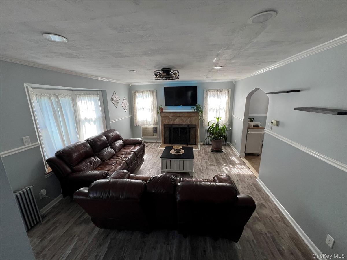 Spacious living area featuring dual dark leather sectional seating arrangements, wood-finish flooring throughout, and a fireplace with stone surround