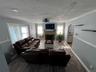 Spacious living area featuring dual dark leather sectional seating arrangements, wood-finish flooring throughout, and a fireplace with stone surround