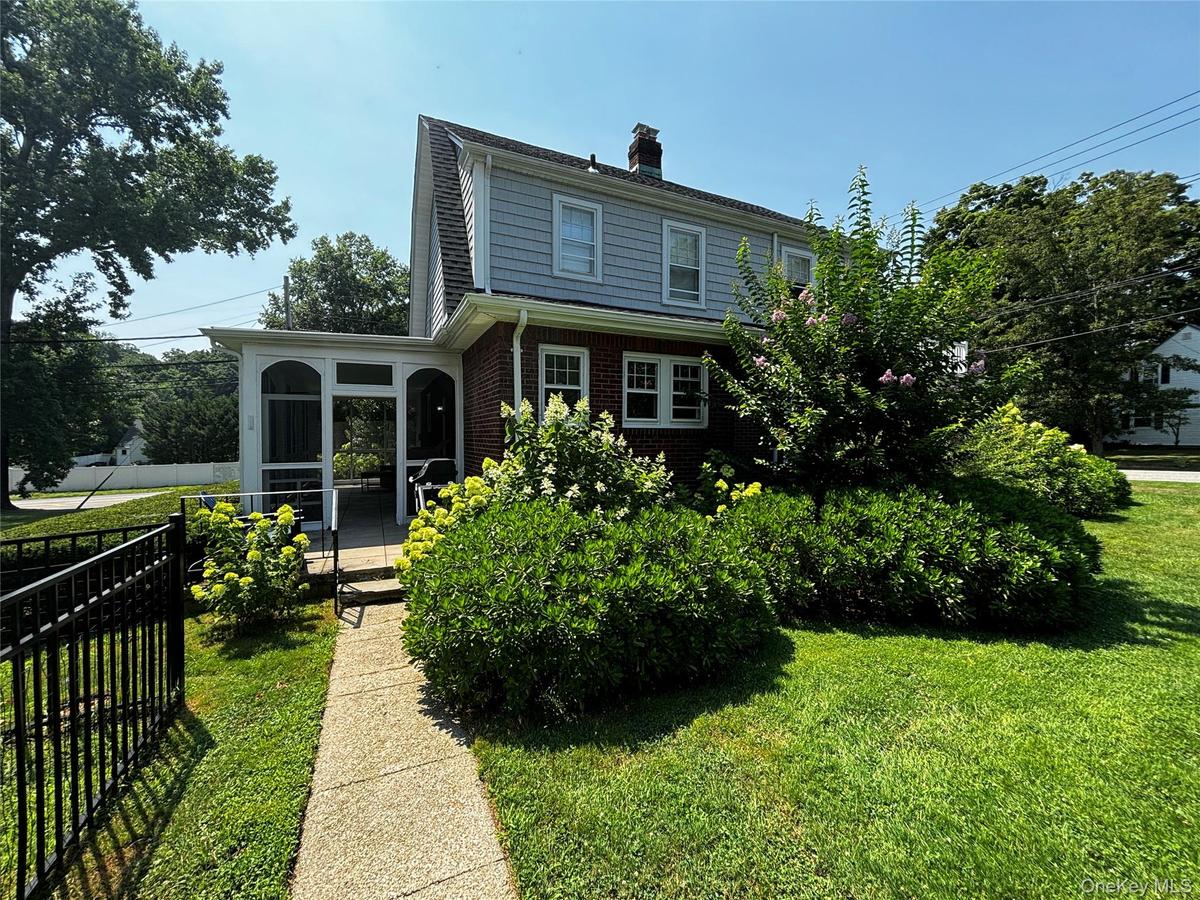 Rear view of house featuring a chimney, brick siding, a sunroom, a yard, and fence